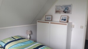 Quarto com cama, guarda-roupa, abajur e duas molduras na parede.