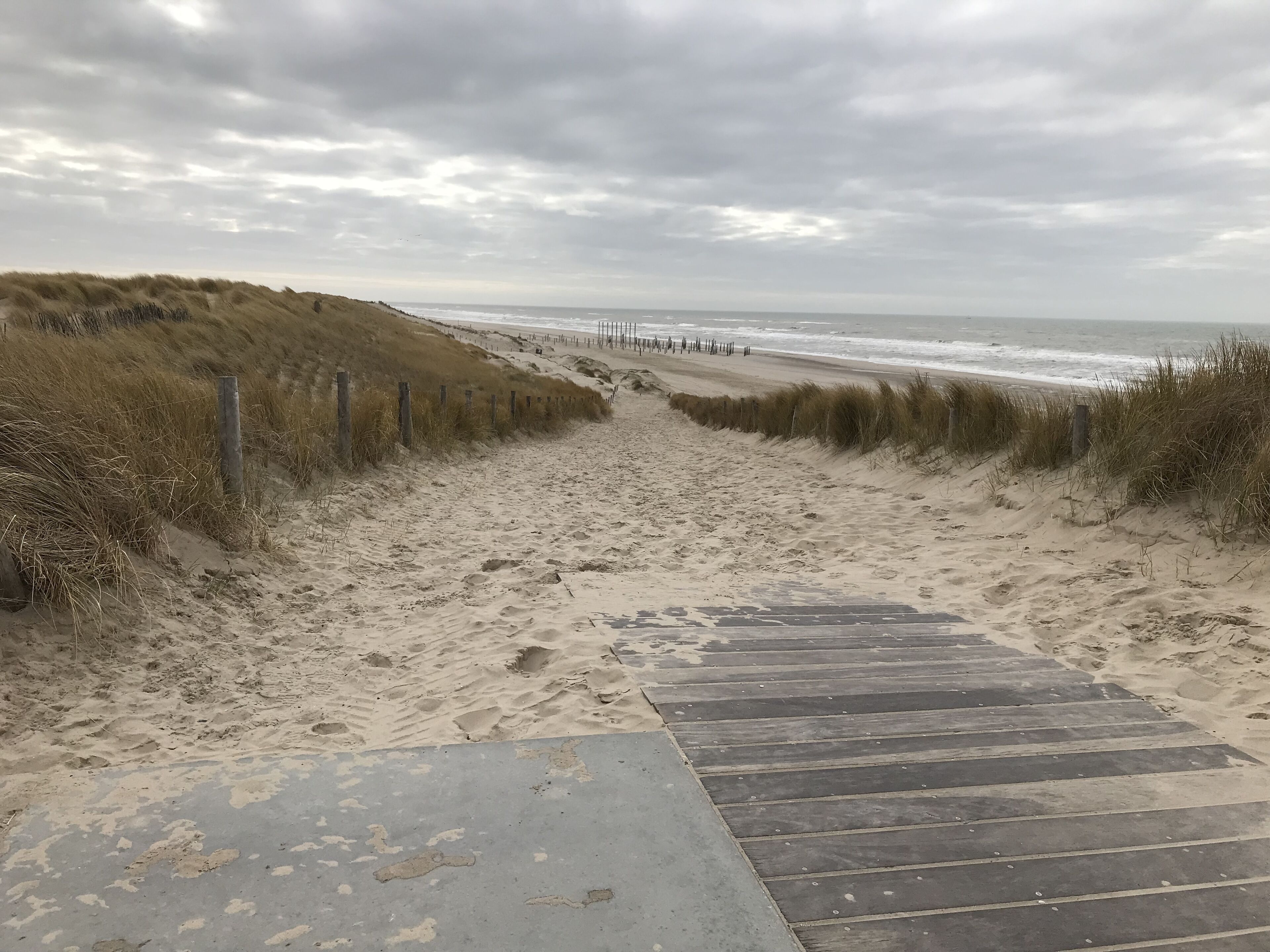 Ein sandiger Strandweg führt zum Meer, mit Holzstufen und einem Holzzaun.