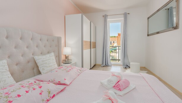A bedroom with a tufted headboard, floral bedding, a bedside table with a lamp, and a view of a balcony. - Family-friendly, quiet location, near the beach, barbecue in the garden, (Poreč)