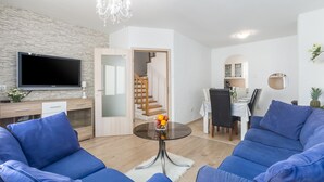 A modern living room with a flat-screen TV, blue sofas, a glass coffee table with fruit, and a staircase leading to a dining area. - Family-friendly, quiet location, near the beach, barbecue in the garden, (Poreč)