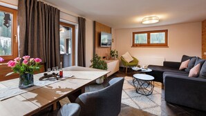 Ein modernes Wohnzimmer mit Essbereich, ausgestattet mit einem Holztisch, grauen Stühlen, einem schwarzen Sofa und einem kleinen runden Couchtisch.