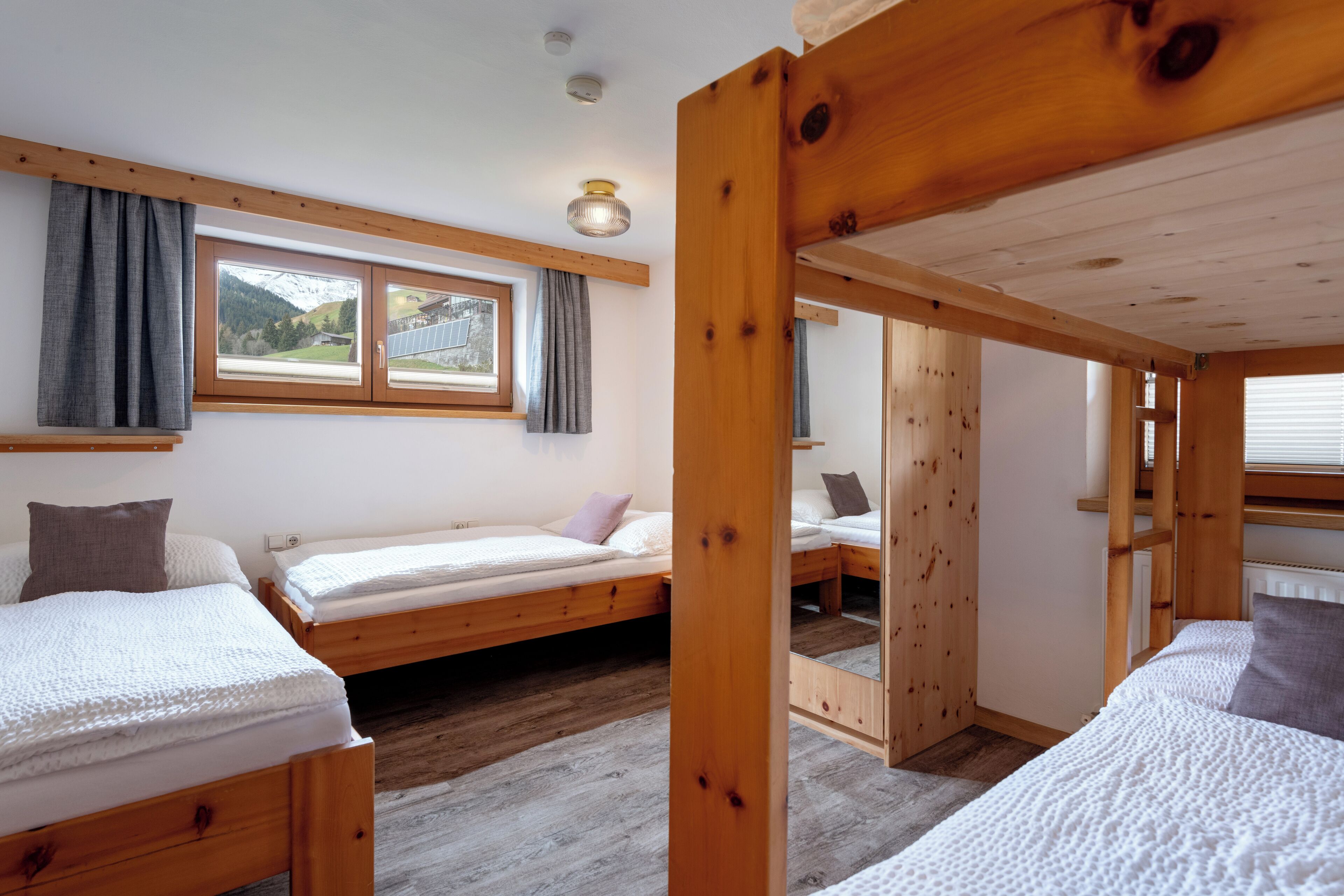 Une chambre avec deux lits superposés en bois, une fenêtre avec des rideaux, un miroir et un radiateur.