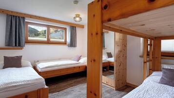 Une chambre avec deux lits superposés en bois, une fenêtre avec des rideaux, un miroir et un radiateur.
