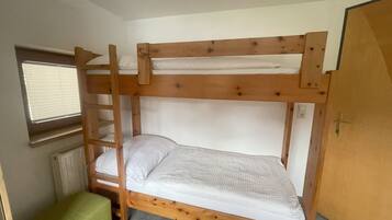 Ein Stockbett mit einer Leiter, ein kleiner grüner Stuhl und ein Fenster mit Jalousien.