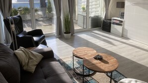 A modern living room with a sofa, two round wooden tables, a potted plant, and a view of the outside through large sliding glass doors. - Modern, premium lake view vacation apartment over 2 floors (Waldeck -Scheid)