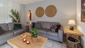 A modern living room with a grey sofa, a wooden coffee table with candles, a lamp, and a woven wall hanging. - Awesome home in Wemeldinge with kitchen (Wemeldinge)