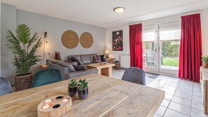 A cozy living room with a dining table, sofas, and a large window with red curtains. - Awesome home in Wemeldinge with kitchen (Wemeldinge)