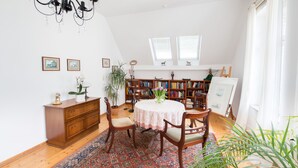 A room with a wooden floor, a round table with a lace tablecloth, wooden chairs, a chandelier, a bookshelf, and a window with blinds. - Apartment Hörster in the center of Detmold (Detmold)