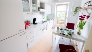 A modern kitchen with white cabinets, a dining table set for four, and a red chair. - Apartment Hörster in the center of Detmold (Detmold)