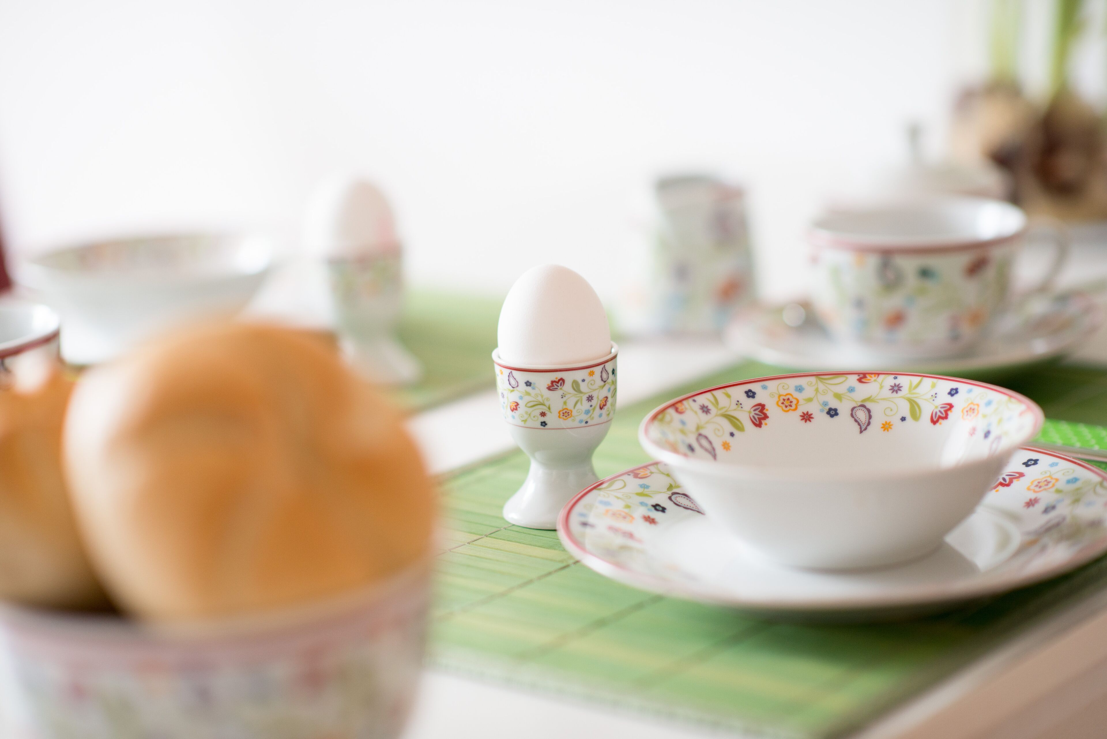 Une table avec un set de table vert, des tasses à thé blanches ornées de motifs floraux et une théière blanche.