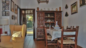 A dining area with a wooden table and chairs, a cabinet with decorative items, and a chair with a cushion.
