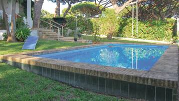 A rectangular swimming pool with a tiled edge, surrounded by a grassy lawn and trees.