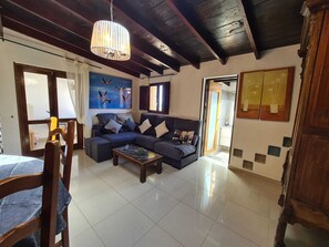 A living room with a dark wooden ceiling, a blue sofa set, a coffee table, and a painting of birds on the wall.