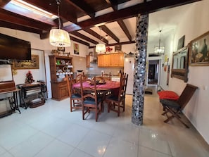 A spacious dining area with a wooden table and chairs, a kitchen with wooden cabinets, and a decorative column.