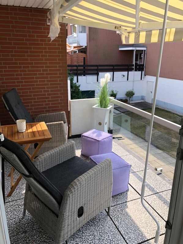 Un patio techado con mobiliario de mimbre, una mesita y una planta en maceta.