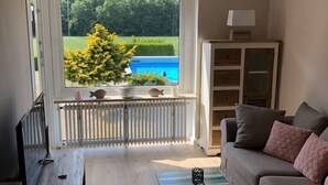 Een woonkamer met uitzicht op een zwembad, een bank, een salontafel, een televisie en een kast.