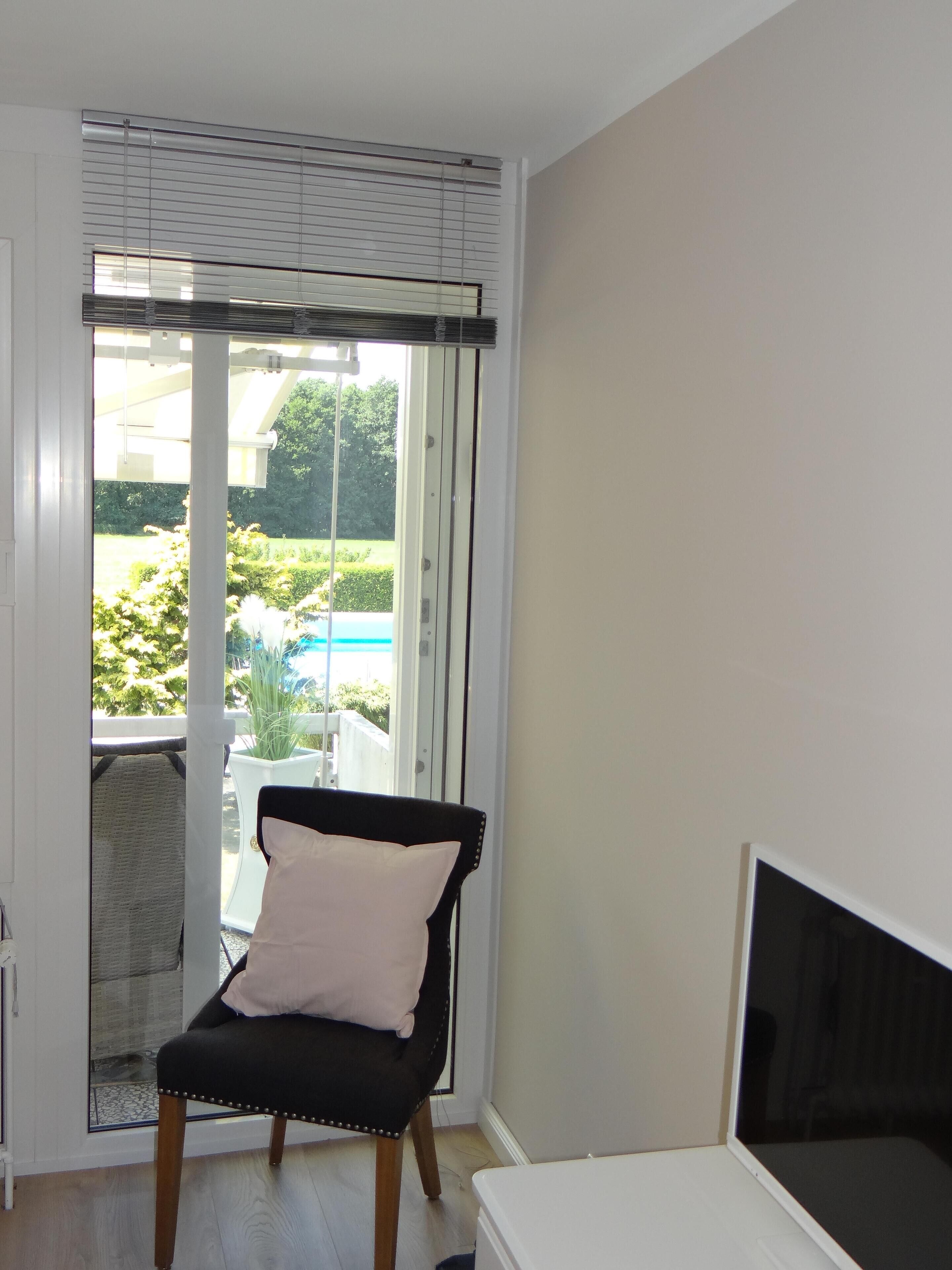 Une pièce dotée d’une porte-fenêtre coulissante donnant sur un balcon, d’une chaise noire avec un coussin et d’une table de chevet blanche.