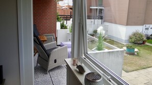 Een balkon met rieten meubilair, uitzicht op een bakstenen muur, en een tuin met potplanten.