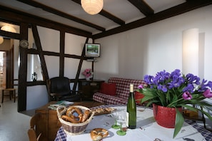 A cozy living room with a wooden table set for a meal, a television, and a vase of purple flowers.