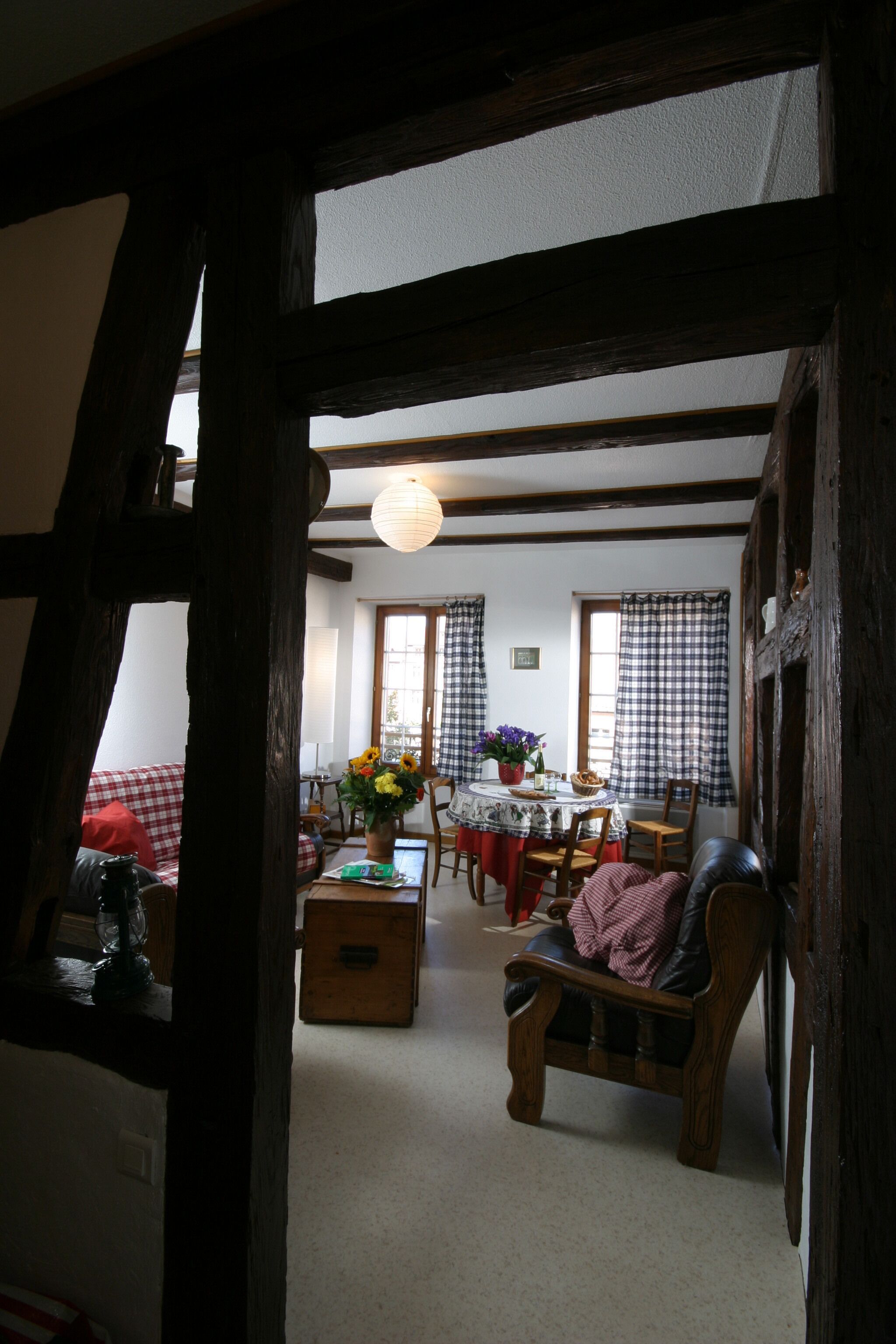 A traditional room with exposed wooden beams, a dining area with a table set for two, and a cozy seating area with a sofa and armchair.