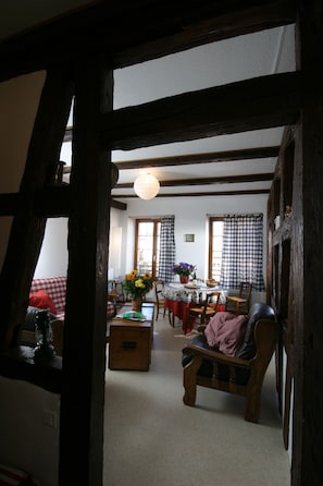 A traditional room with exposed wooden beams, a dining area with a table set for two, and a cozy seating area with a sofa and armchair.