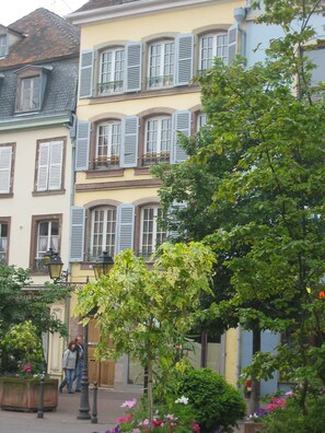 A street with buildings featuring traditional architecture, including shuttered windows and balconies.