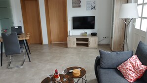 En stue med sofa, sofabord, vinglas, vinflaske, fjernsyn på et stativ og en lampe.