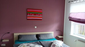 En seng med træramme, knæstøtte og blå madras. Der er et billede hængt på væggen over sengen.