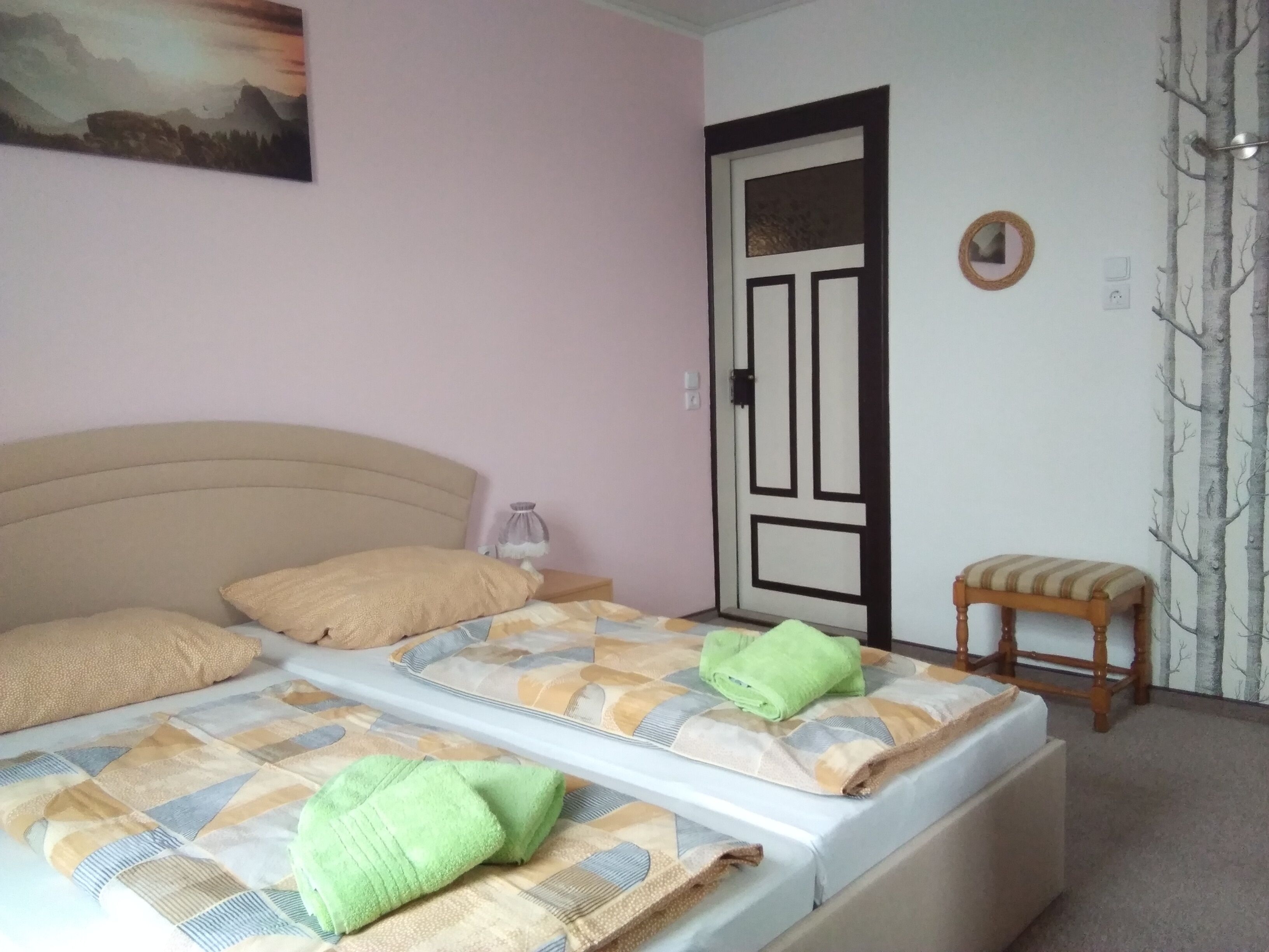 Une chambre à coucher avec un lit, des oreillers, une table de chevet, une chaise, une porte et un mur orné d’un tableau.