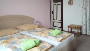 Een slaapkamer met een bed, kussens, een nachtkastje, een stoel, een deur en een muur met een schilderij.
