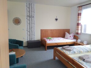A bedroom with a wooden bed, a small round table with a vase, a blue sofa, and a wall-mounted mirror. - Rest and relaxation in a charming nature in every season! (Altenberg)
