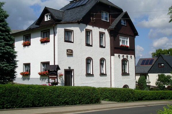 A two-story building with a white facade, multiple windows, and red flower boxes. - Rest and relaxation in a charming nature in every season! (Altenberg)