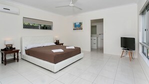 A modern bedroom with a large bed, a ceiling fan, a TV on a stand, and a window. - Connemara (Trinity Beach)