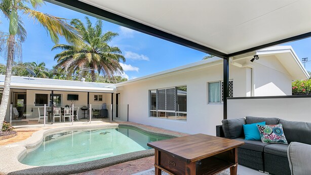 A modern outdoor living area with a pool, a wooden table, and a sofa with cushions. - Connemara (Trinity Beach)