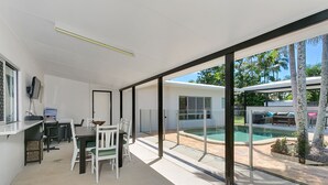 A modern living room with a dining area, large windows, and a view of a swimming pool. - Connemara (Trinity Beach)