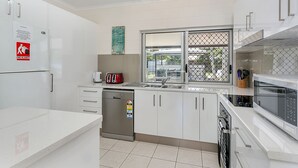 A modern kitchen with white cabinets, stainless steel appliances, and a dishwasher. - Connemara (Trinity Beach)