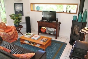 A living room with a sofa, coffee table, television, fireplace, and a window with decorative items.