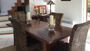 Een eethoek met een houten tafel, rieten stoelen, een vaas met bloemen en een ingelijste foto aan de muur.
