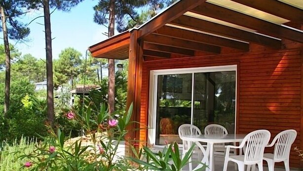 Een houten huis met een overdekte patio, een glazen deur en een tafel met stoelen.