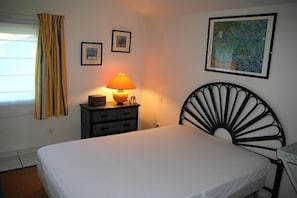 A bedroom with a bed, a nightstand with a lamp, a dresser, and a painting on the wall.
