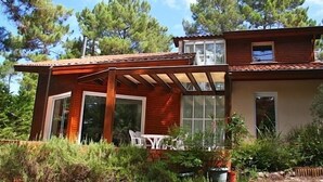 Een houten huis met twee verdiepingen, een terras, grote ramen en een tuin.