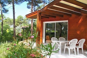 Eine Terrasse im Freien mit Tisch und Stühlen, umgeben von Pflanzen und einer Holzkonstruktion.