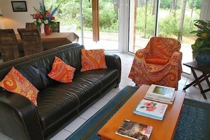 A living room with a black leather sofa, an orange patterned armchair, and a wooden coffee table with magazines. - Beautiful house with idyllic views G0268 (Lacanau)