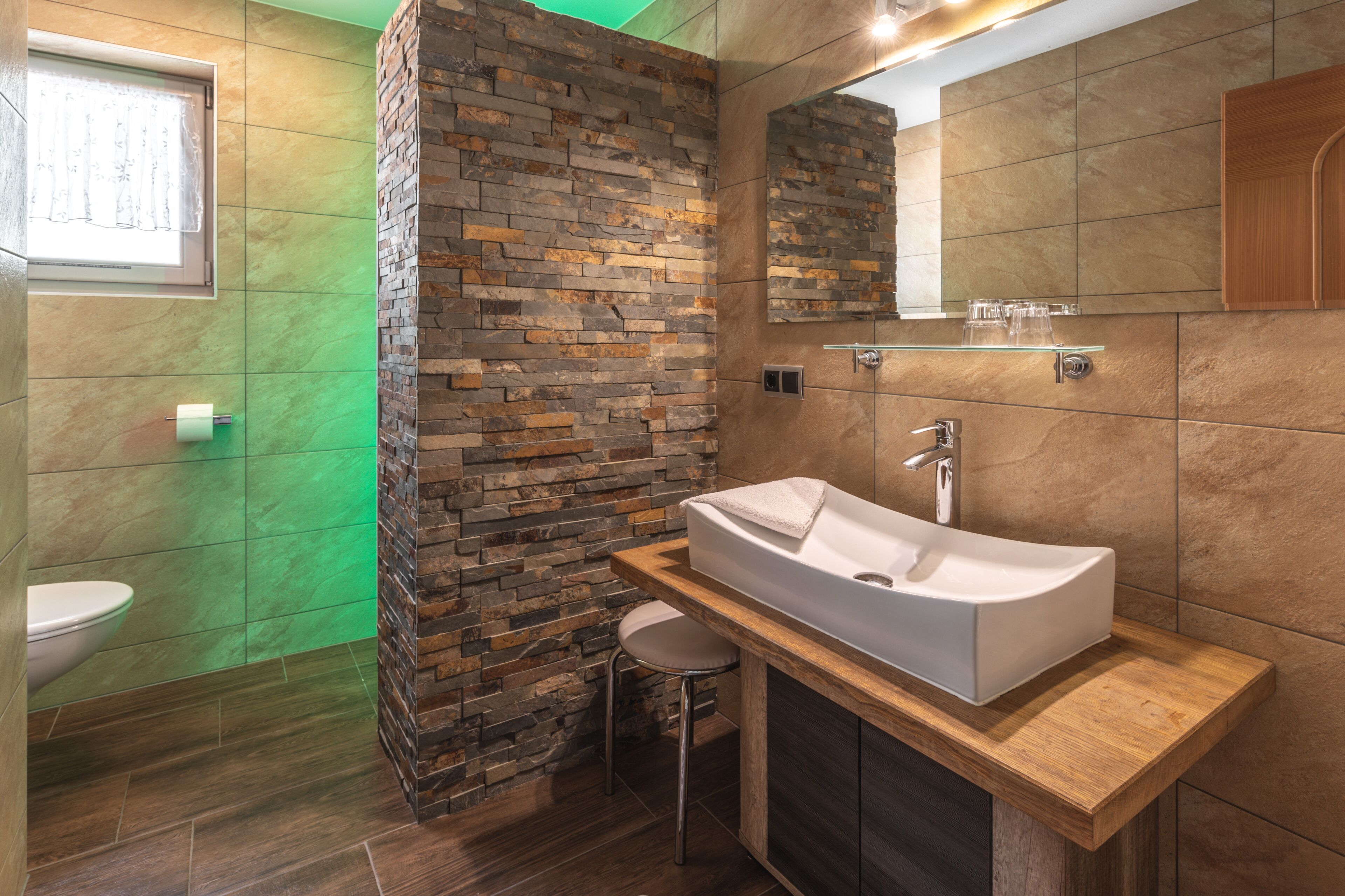 A modern bathroom with a stone wall, a white sink, and a wooden vanity.