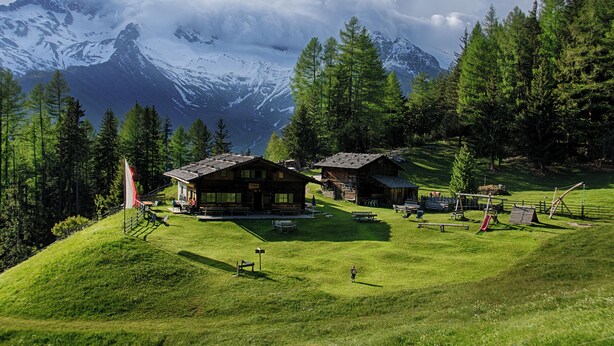 Un chalet de montagne comprenant plusieurs cabanes en bois, un drapeau, des tables de pique-nique et une aire de jeux.