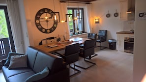 A modern living room with a dining area, kitchen, and a large window with curtains.