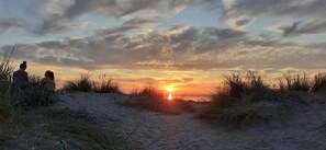 A sunset over a sandy beach with two people sitting on the sand. - Row corner house, in the middle of Norddeich, quiet location, family friendly, WiFi free (Norden-Norddeich)