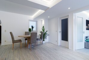 A modern dining area with a wooden table and chairs, a potted plant, and a door with frosted glass panels.