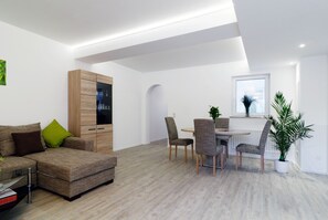 A modern living room with a sofa, dining table, chairs, and a potted plant.