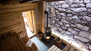 A wooden interior with a stone wall, a fireplace, and wooden benches.